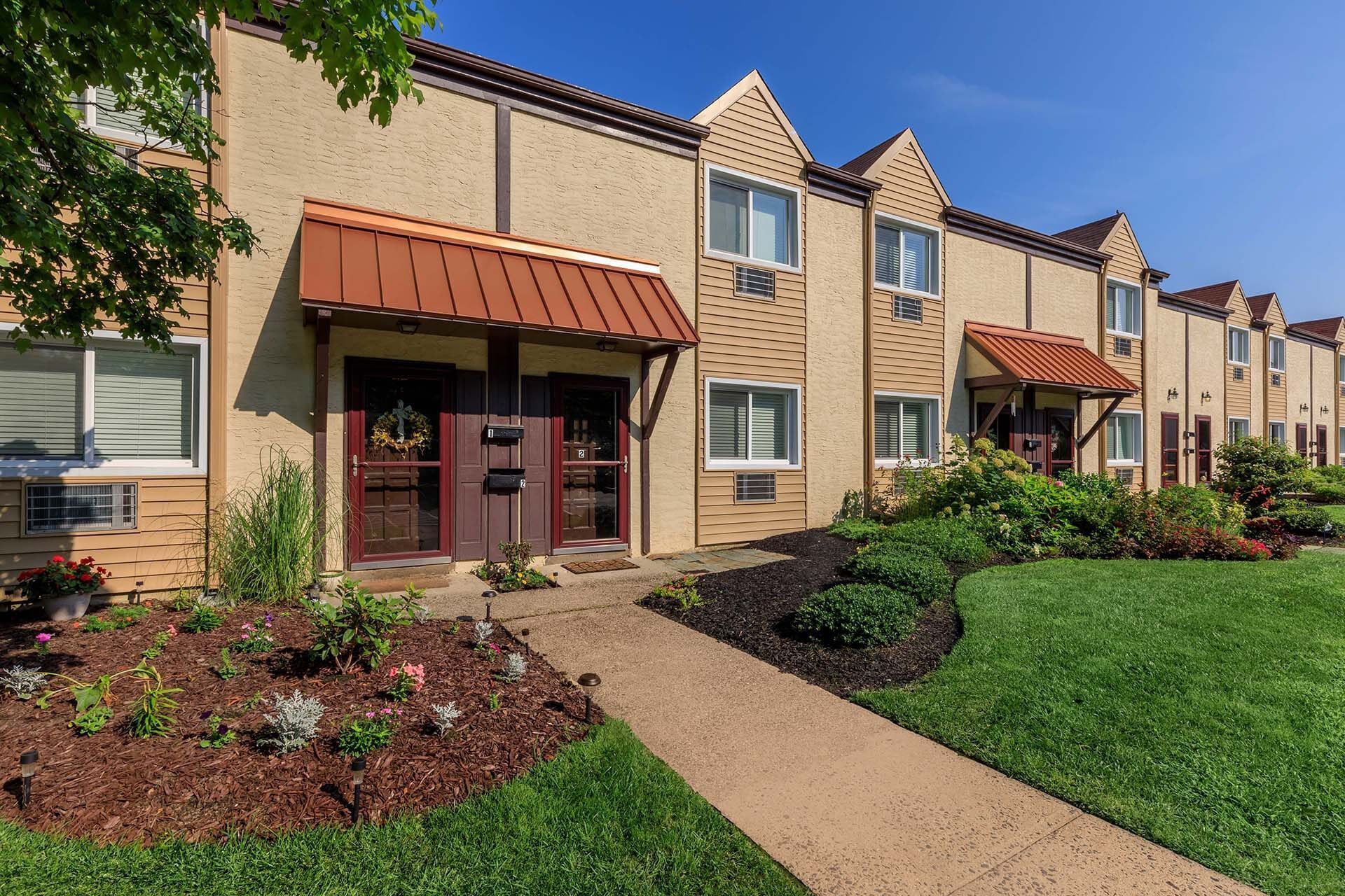 Exterior view of a townhouse-style apartment complex with covered entry doors and landscaped front yard at The Addison, offers apartments for rent in North Wales, PA.