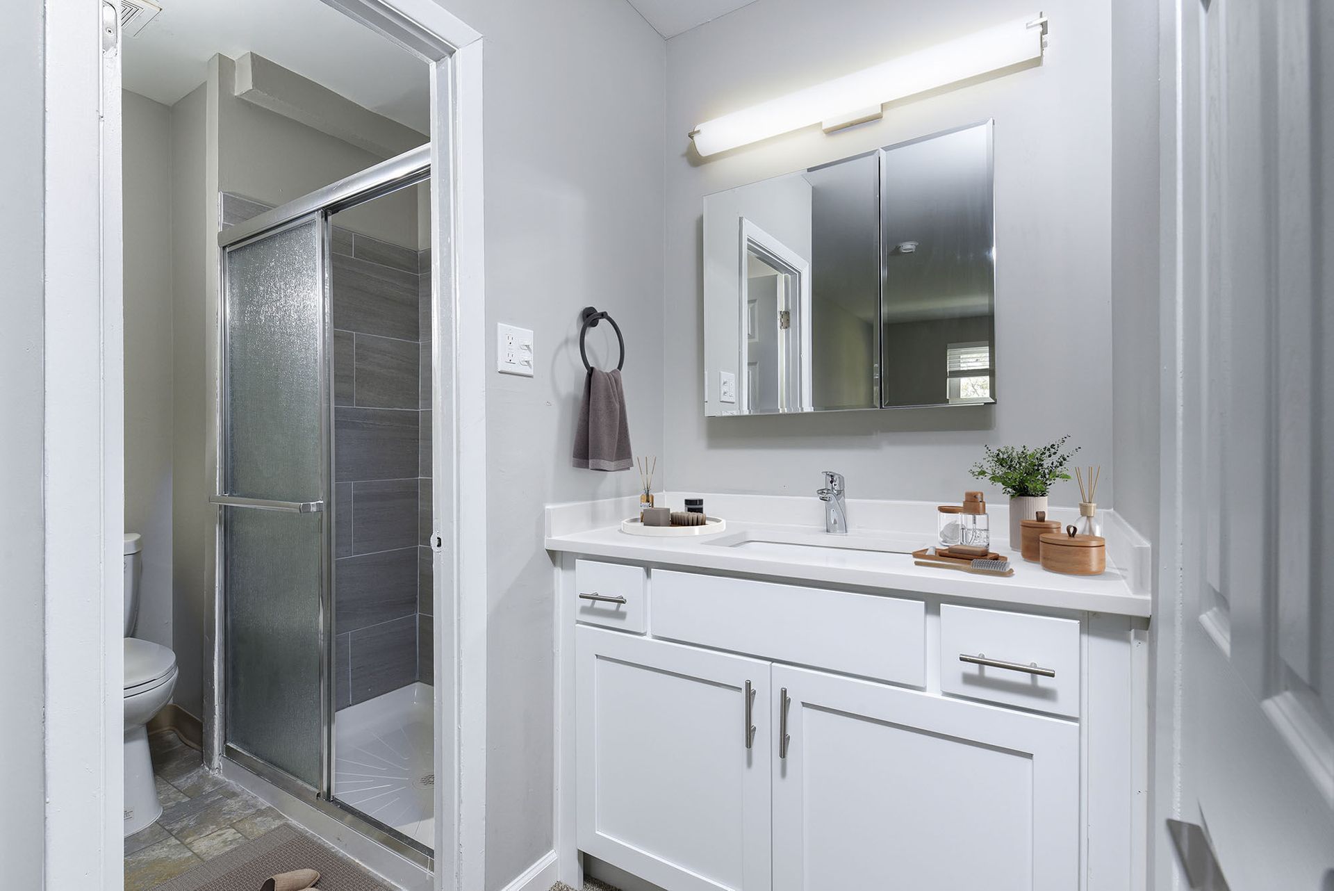 Bathroom vanity with white cabinetry, large mirror, towel ring, and glass shower enclosure at The Addison, offers townhomes in North Wales, PA.
