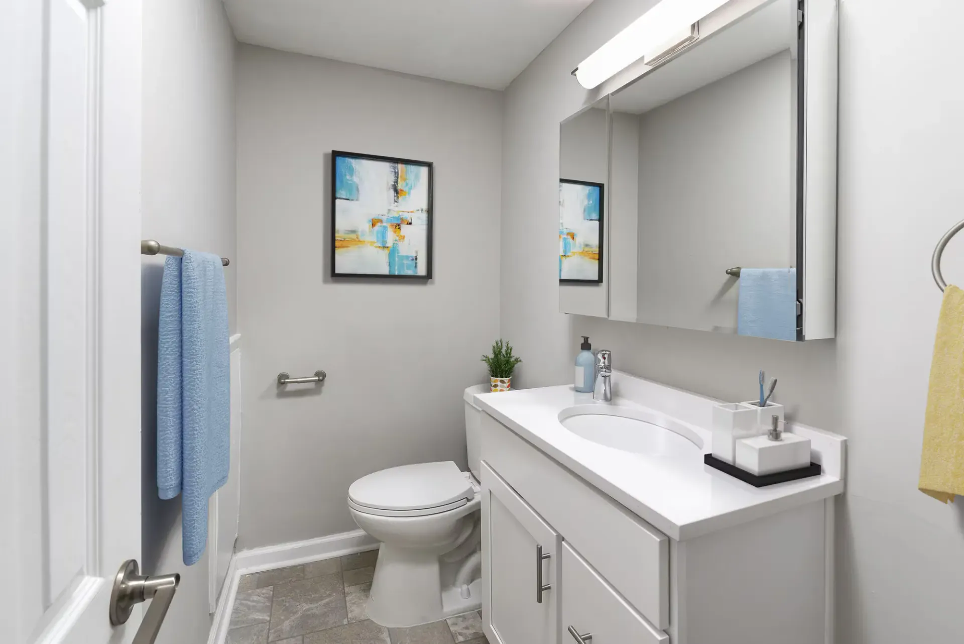Modern apartment bathroom with sink, large mirrored cabinet, toilet, and blue towels at The Addison, offers townhomes in North Wales, PA.