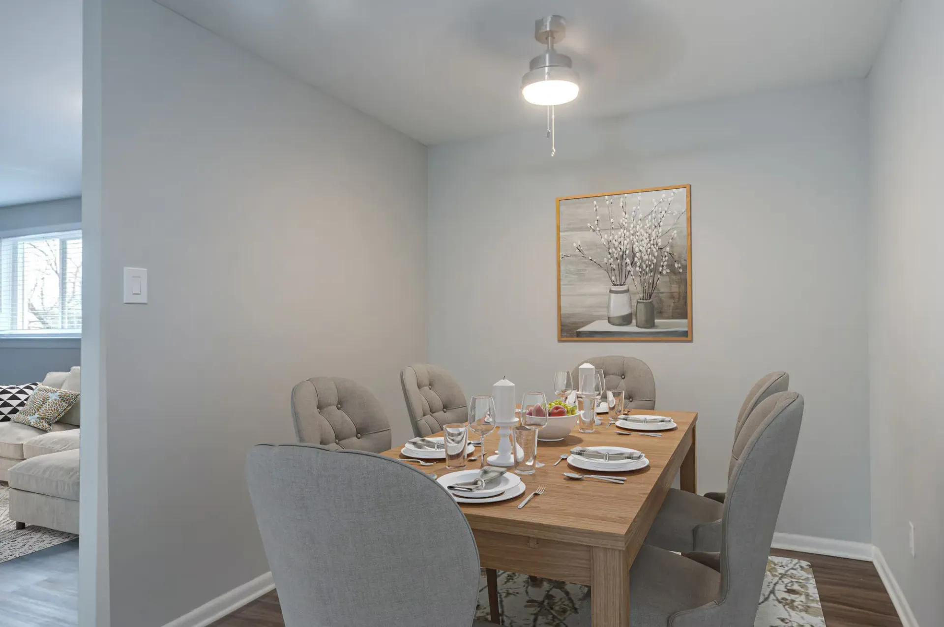 Dining area in a modern apartment with a wooden table, gray upholstered chairs, and wall art at The Addison, offers townhomes for rent in North Wales, PA.
