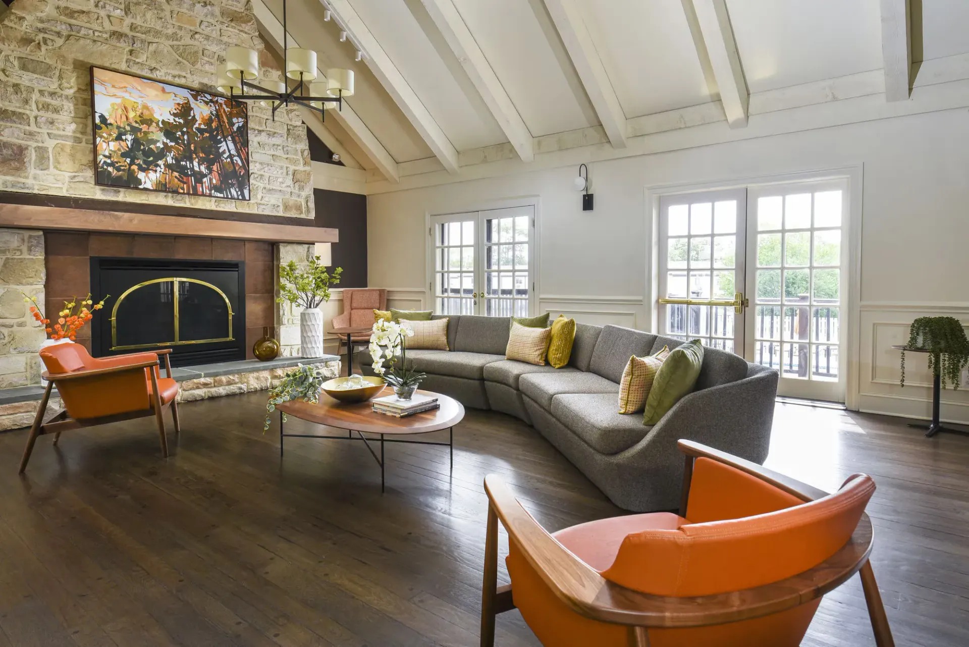 Bright apartment living room with a stone fireplace, gray sectional, and orange accent chairs at The Addison, offers townhomes for rent in North Wales near Delaware Valley University.