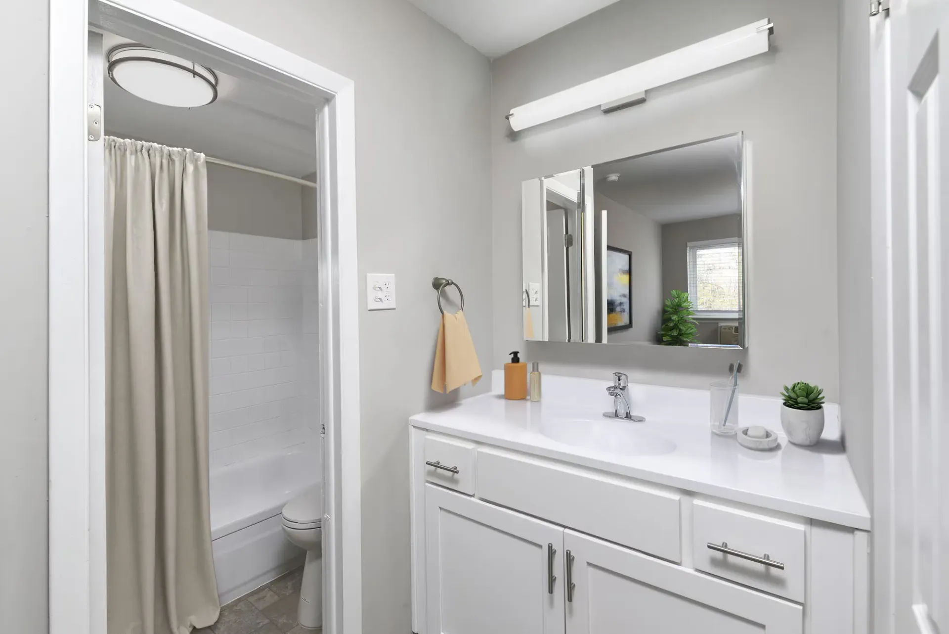 Bathroom vanity with white countertop, sink, mirror, and shower with beige curtain at The Addison, offers townhomes for rent in North Wales near Delaware Valley University.