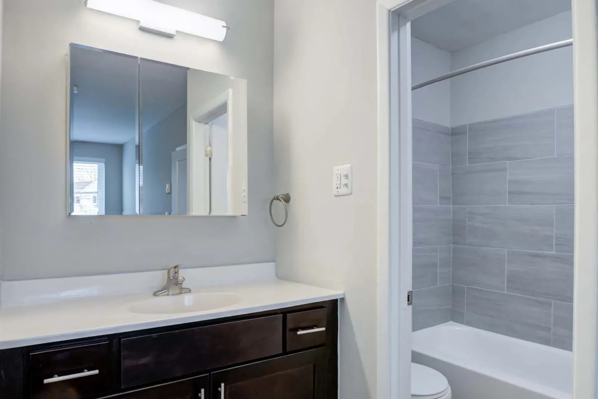 Bathroom with dark wood vanity, white countertop, mirror, and a tiled shower at The Addison, offers apartments in North Wales, PA.