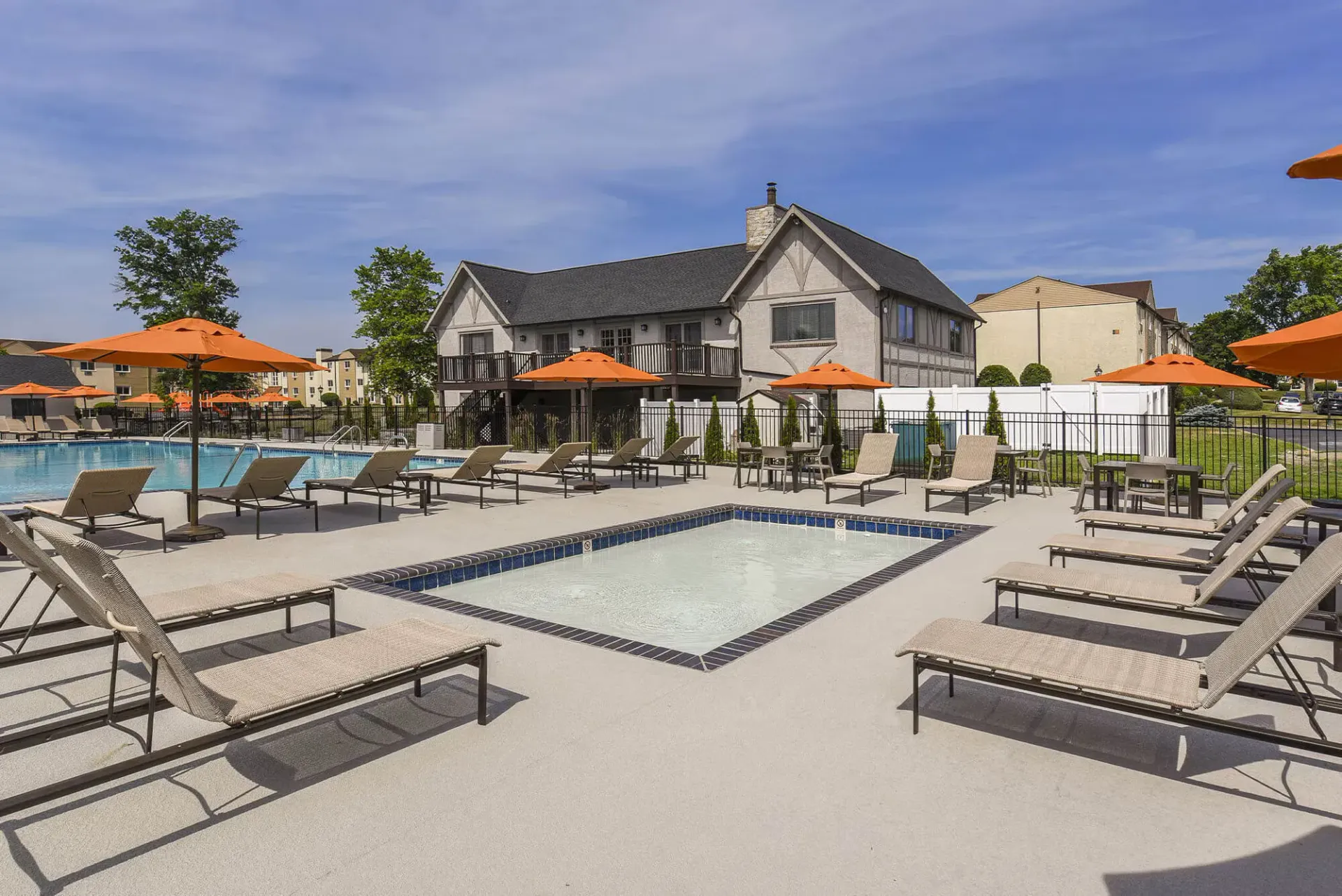 Outdoor community pool area with lounge chairs, orange umbrellas, and a surrounding fence at The Addison, offers apartments for rent in North Wales, PA.