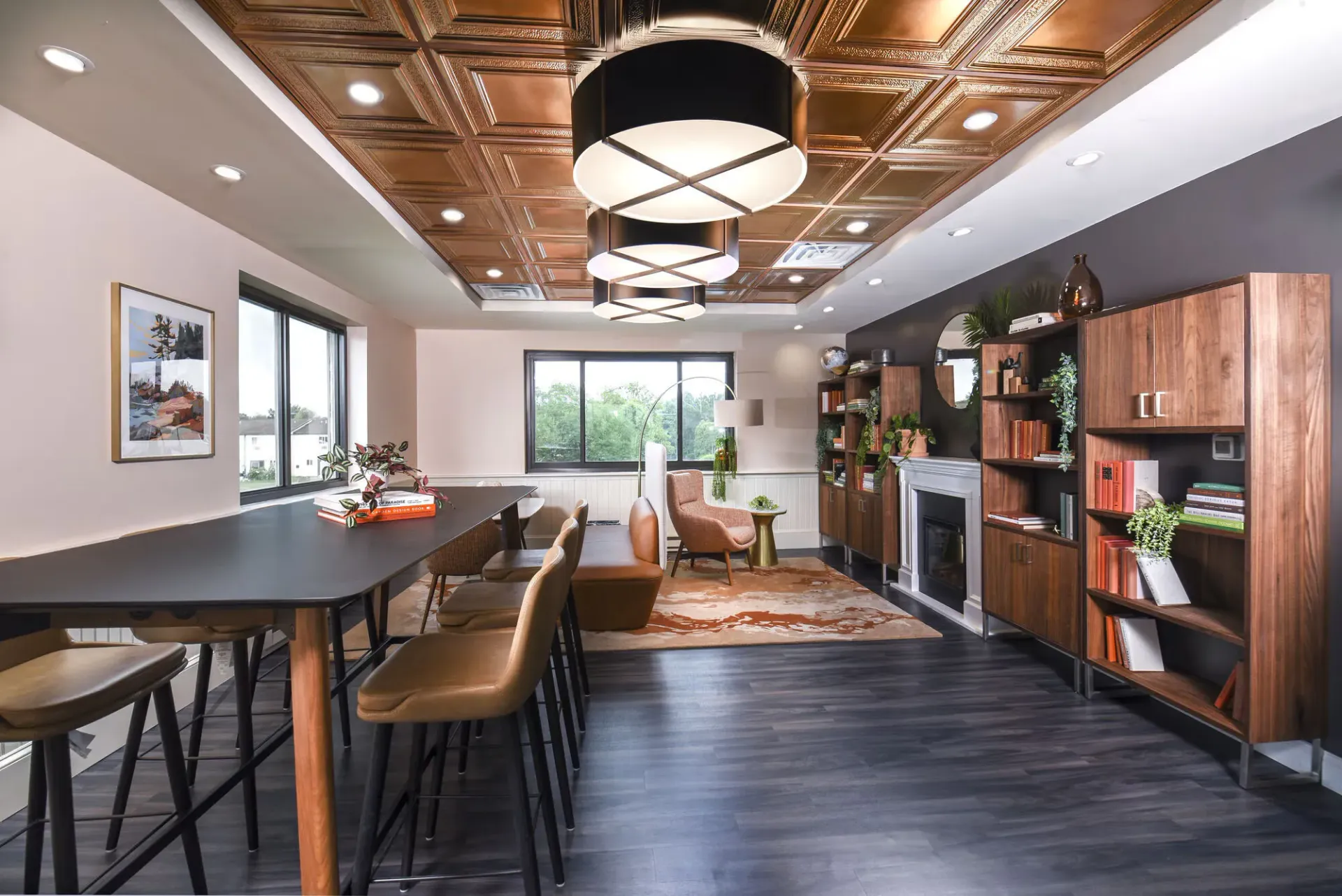 Communal lounge with wood bookshelves, a fireplace, and seating under decorative ceiling lights at The Addison, offers townhomes for rent in North Wales, PA.