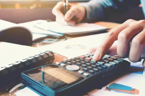 Person using a calculator while writing notes, likely during financial calculations.