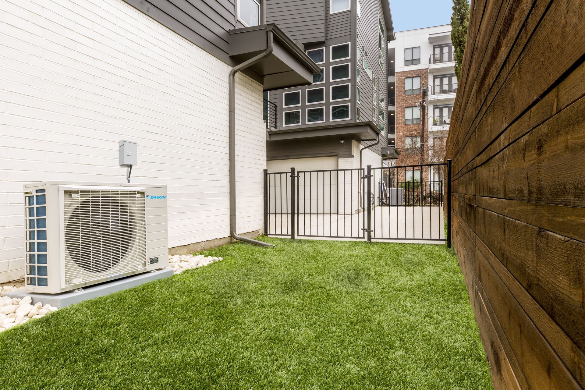 A large Daikin Fit air conditioner is sitting on the side of a building next to a fence.