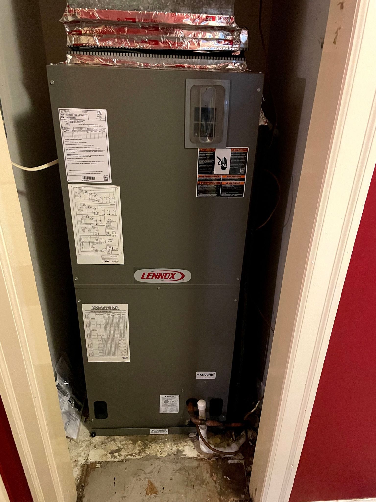 Lennox HVAC unit in a utility closet with ductwork, set against red and beige walls.