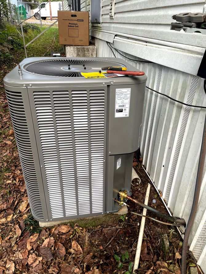 Outdoor air conditioning unit next to a house with tools on top, brown leaves and grass on the ground.