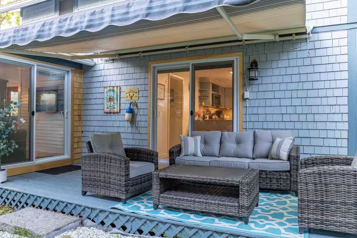 Covered patio with wicker seating, blue patterned rug, and sliding glass doors to a home interior