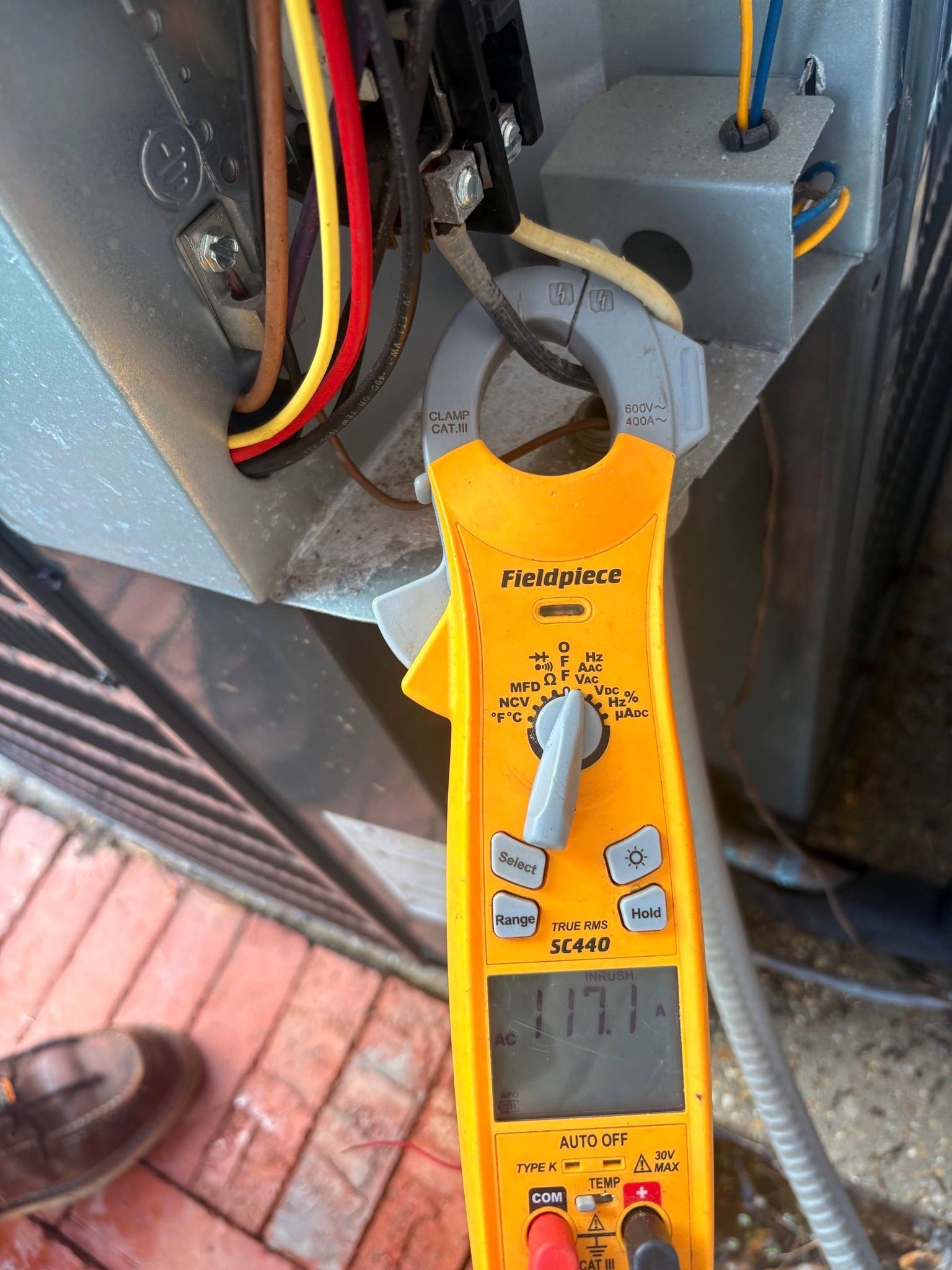 Yellow clamp meter attached to electrical wires inside a panel, reading 277 volts.