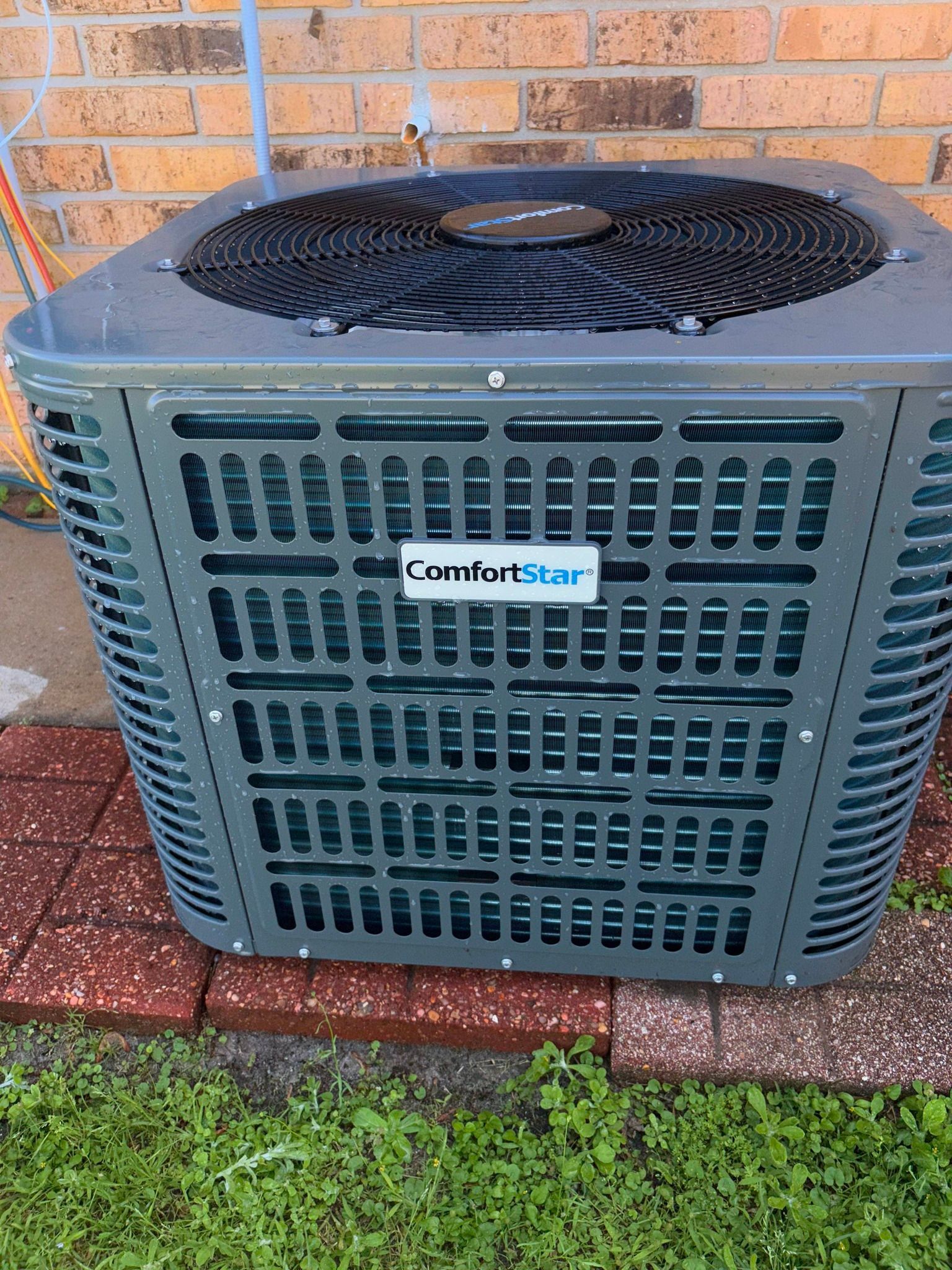 Outdoor ComfortStar air conditioner unit beside a brick wall on a grassy lawn.