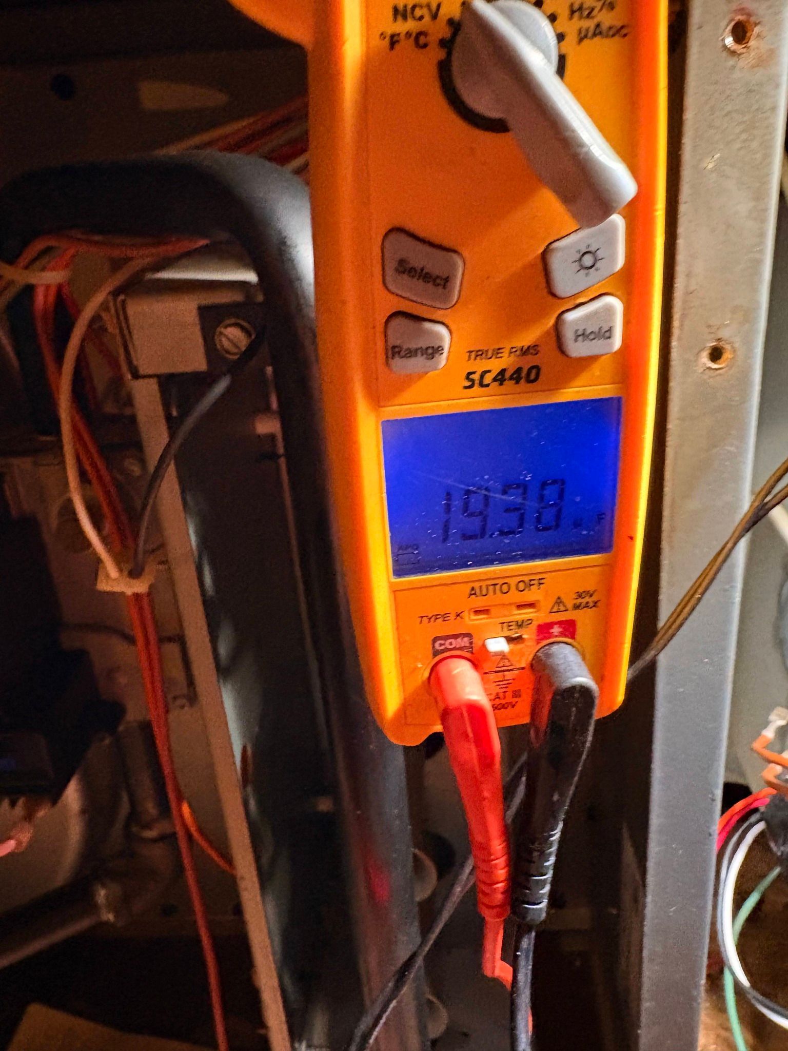 Digital multimeter with blue display and red probes measuring an electrical panel.