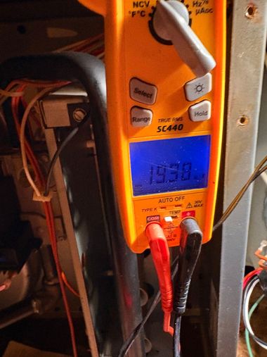 Digital multimeter with blue display and red probes measuring an electrical panel.