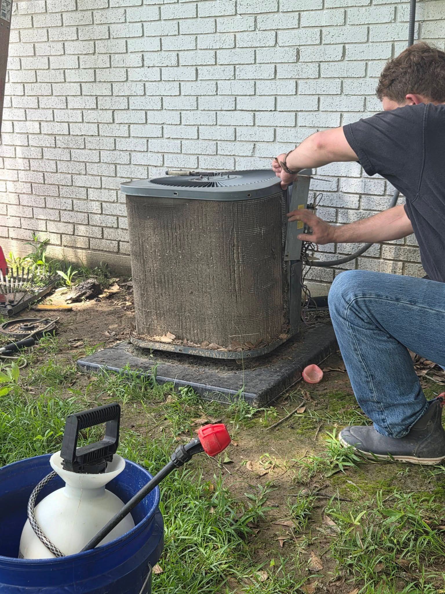 Person using a tool near a large metal drum against a brick wall outdoors