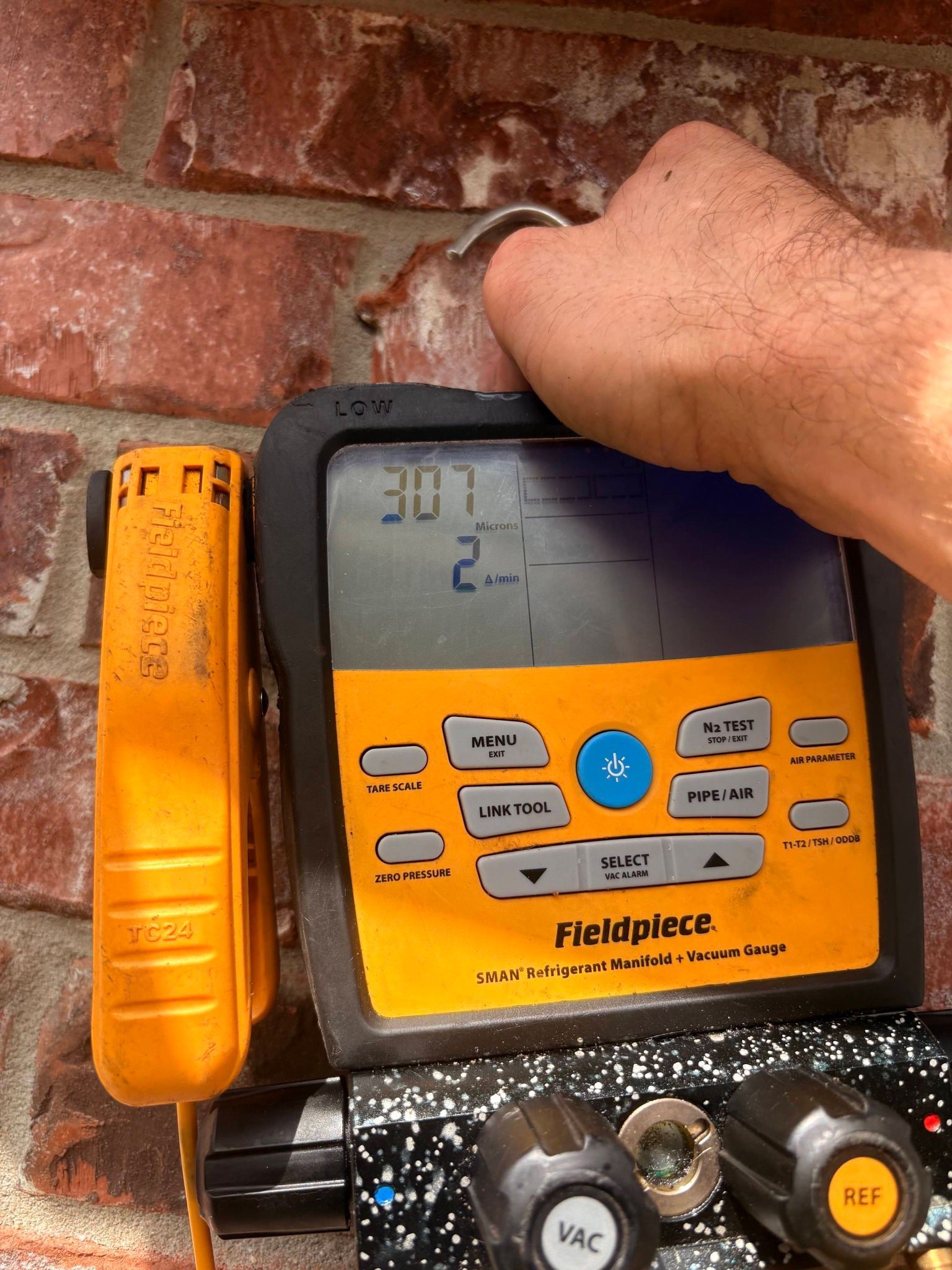 Hand holding a yellow Fieldpiece meter against a brick wall, showing a digital reading.