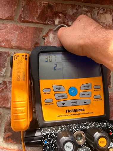 Hand holding a yellow Fieldpiece meter against a brick wall, showing a digital reading.