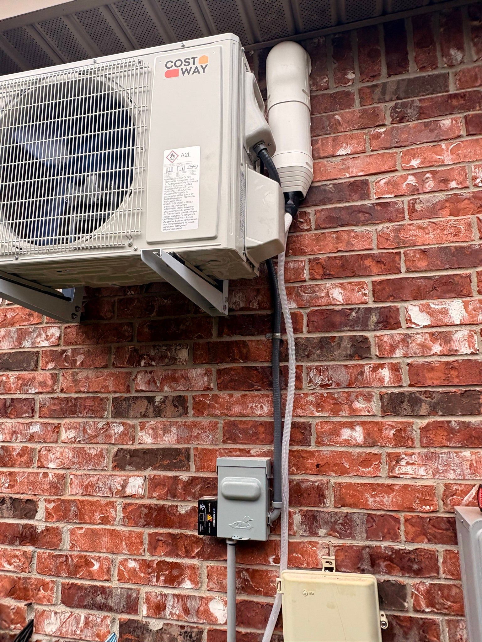 Outdoor air conditioner unit mounted on a brick wall with exposed conduit and electrical boxes