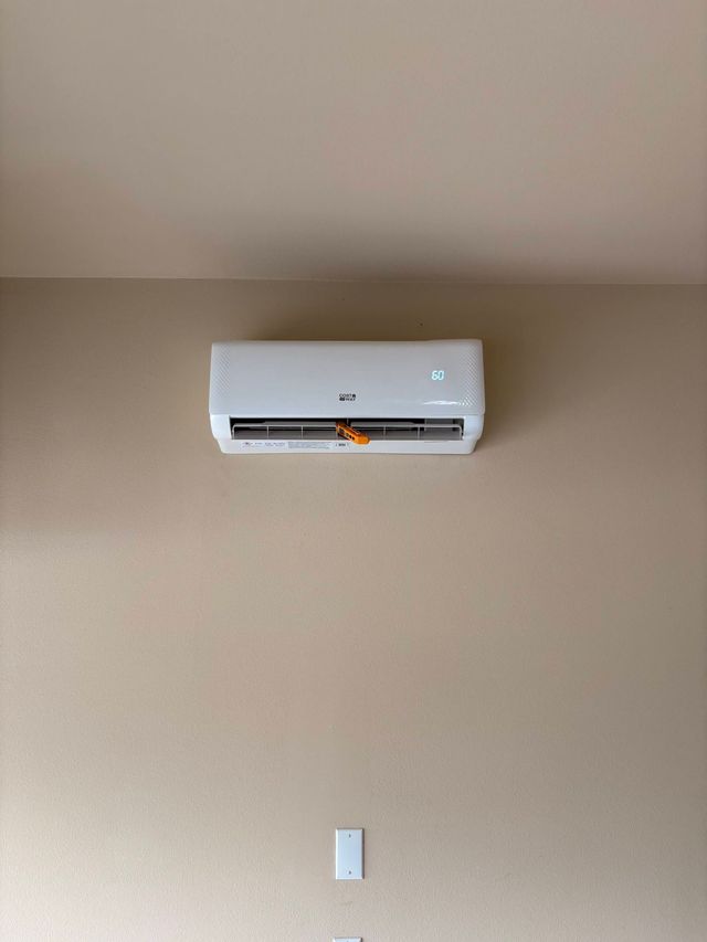 Wall-mounted white air conditioner above a light switch on a beige wall.