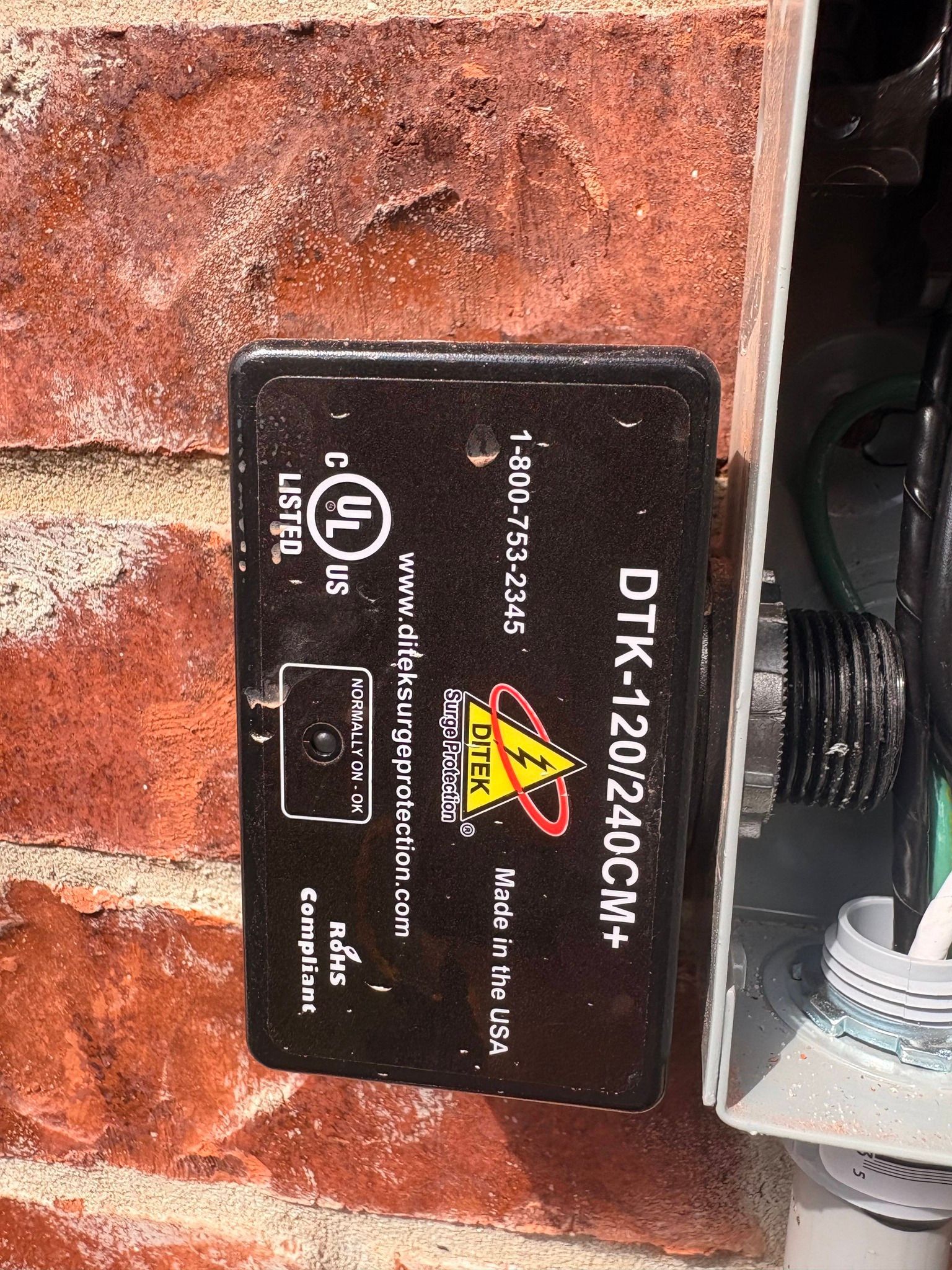 Black electrical device mounted on a wall, with warning label and connected cable.