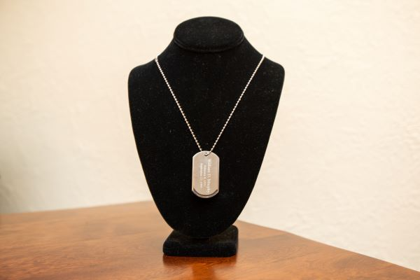 A black mannequin is wearing a dog tag necklace