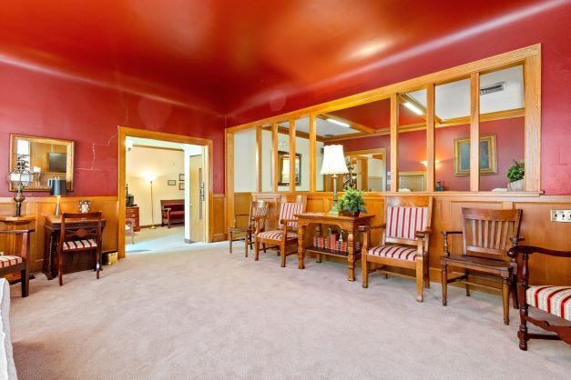 A living room with red walls , chairs , a table and a mirror.