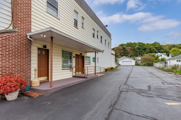 A building with a porch and a parking lot in front of it.
