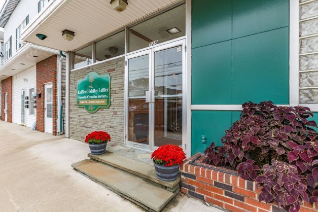 A green and brick building with flowers in front of it.
