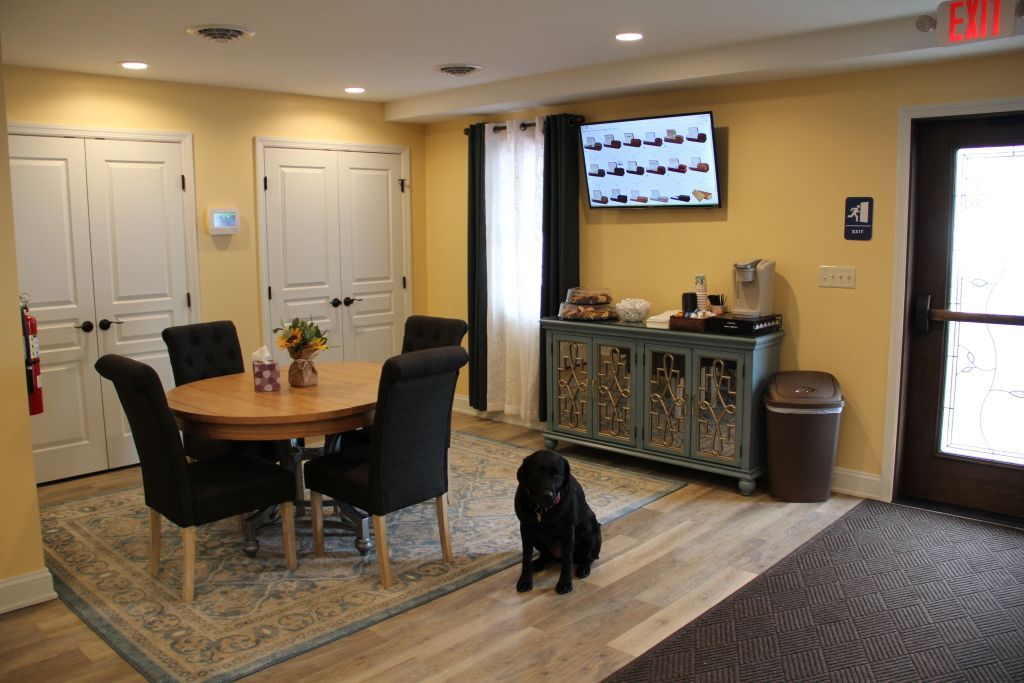 A dog is standing in a living room next to a table and chairs.