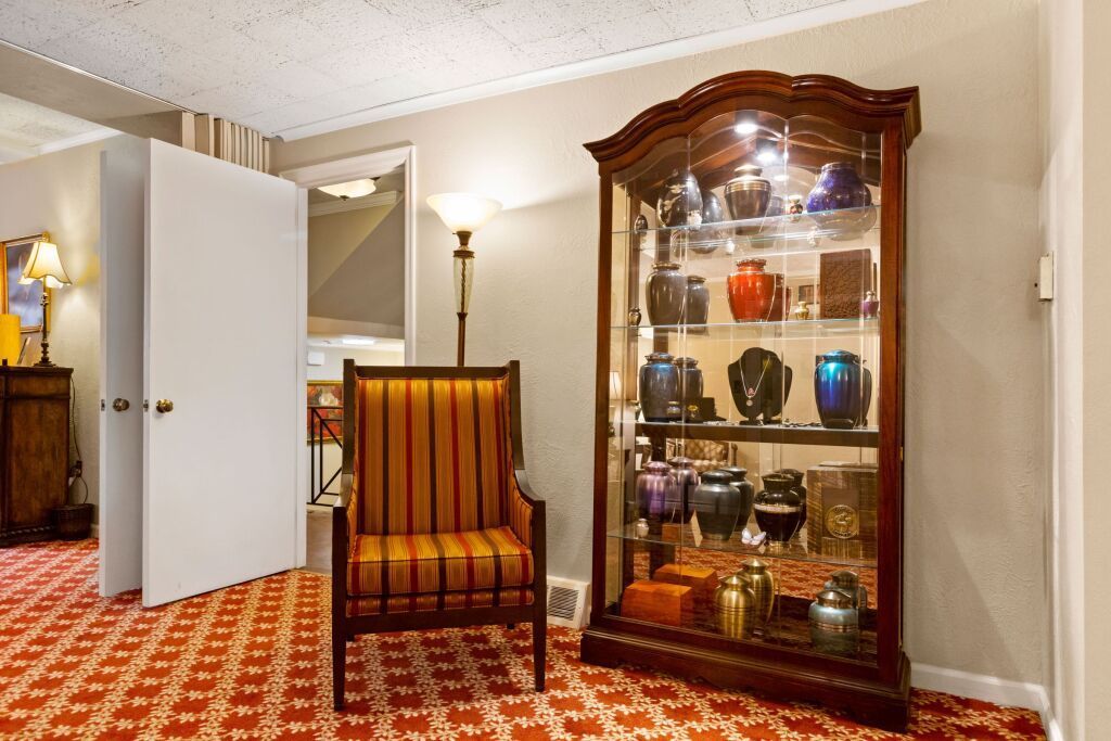 A living room with a chair and a glass cabinet filled with urns.