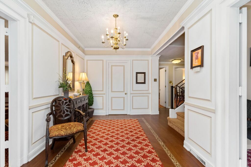 A hallway in a house with a red rug and a chandelier.