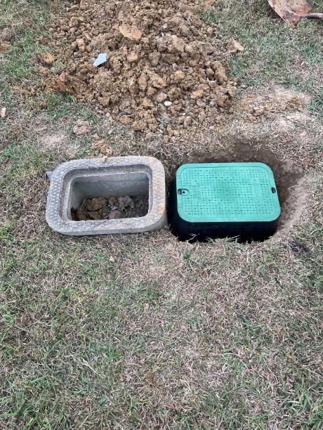 Two rectangular utility boxes in grass, one open, one closed. A pile of dirt and a shovel are visible.