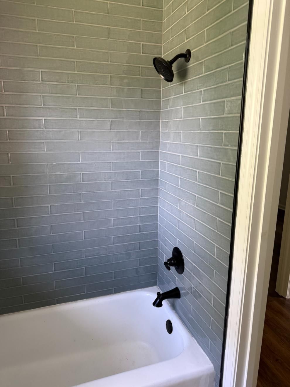 Gray tiled shower with black fixtures and a white bathtub.