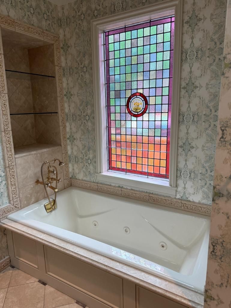 A built-in white jacuzzi tub with a stained glass window above it, and a built-in shelf.