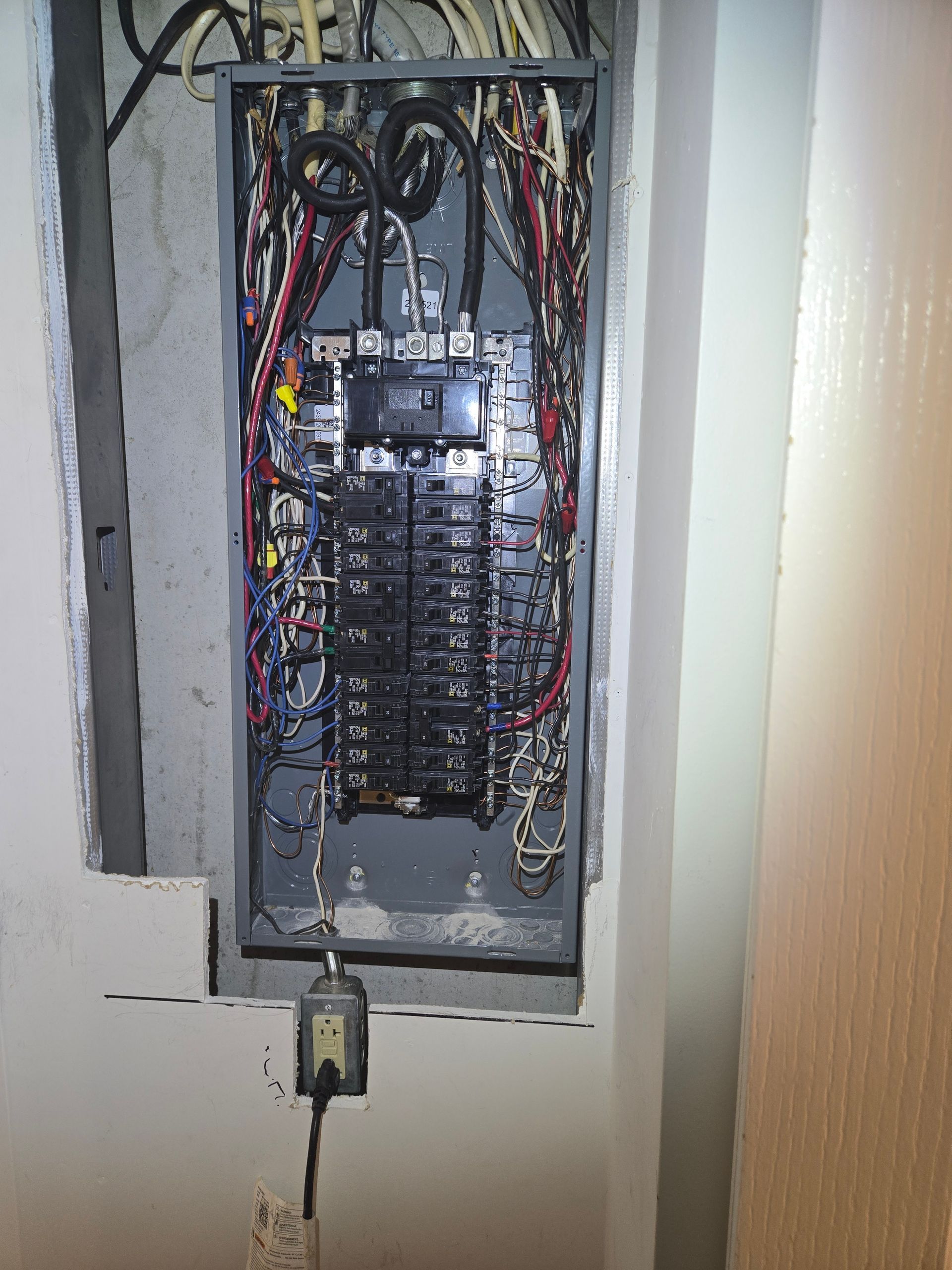 Electrical panel with numerous wires and circuit breakers. Gray metal box, cords, and plug visible.