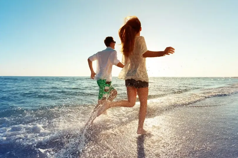 Pareja corriendo por la orilla del mar al atardecer en San Andrés, disfrutando de un momento romántico cerca del Hotel Aquamare.