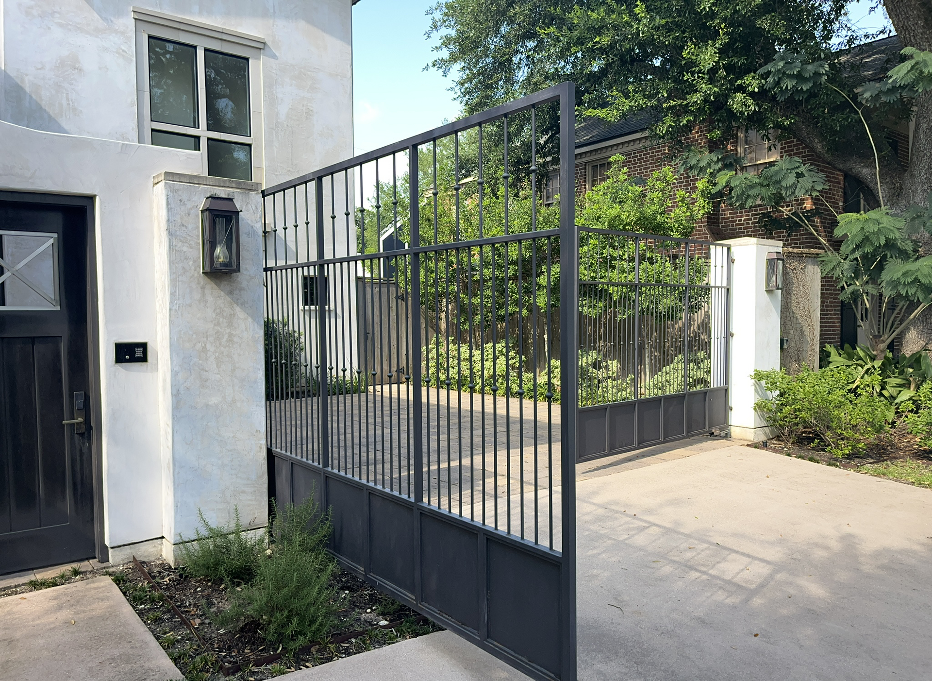 A wrought iron gate with stucco column and keypad remote entry at a home driveway.