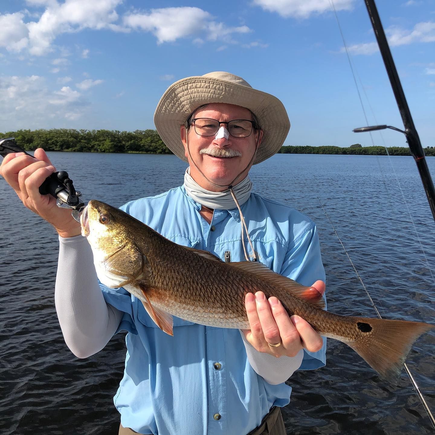 Man in hat holding a redfish on a boat, sunny day.