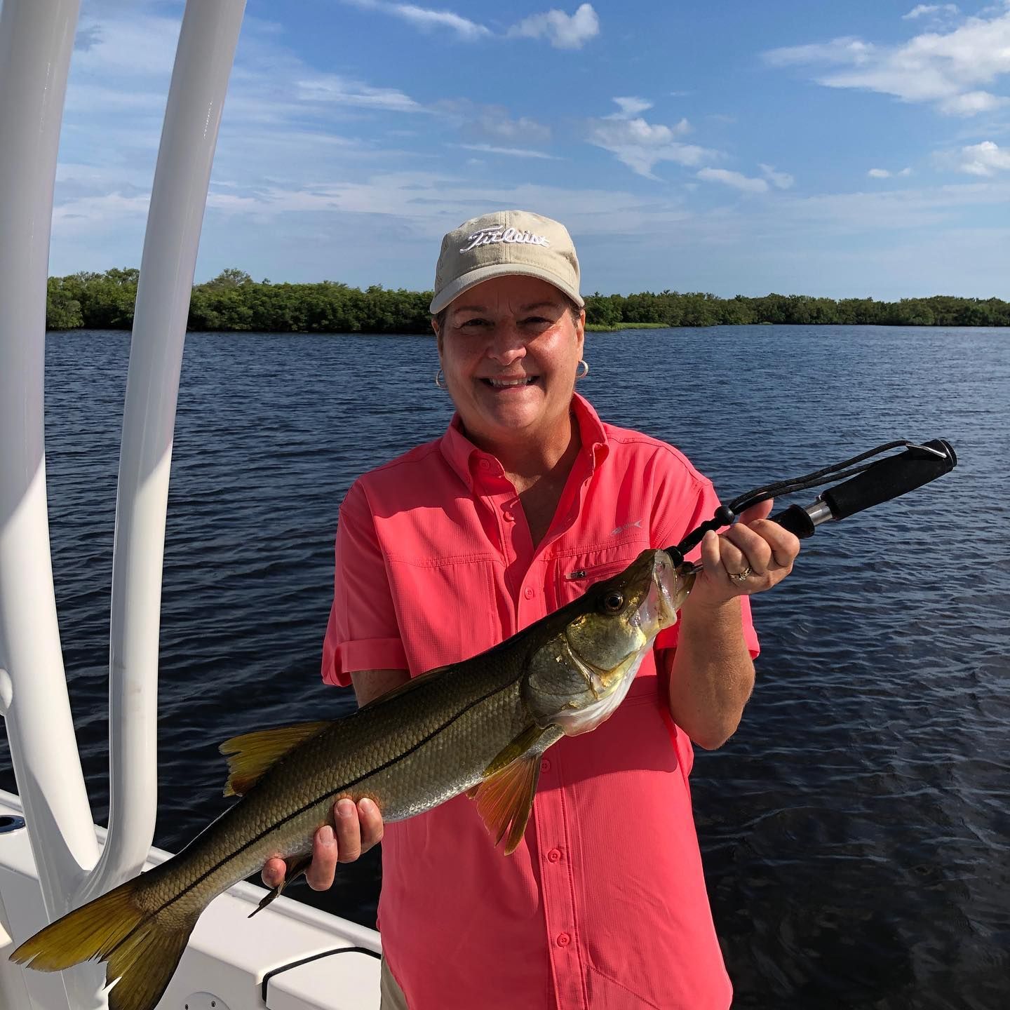 Woman on a boat holding a snook she caught, with water and mangroves in the background.
