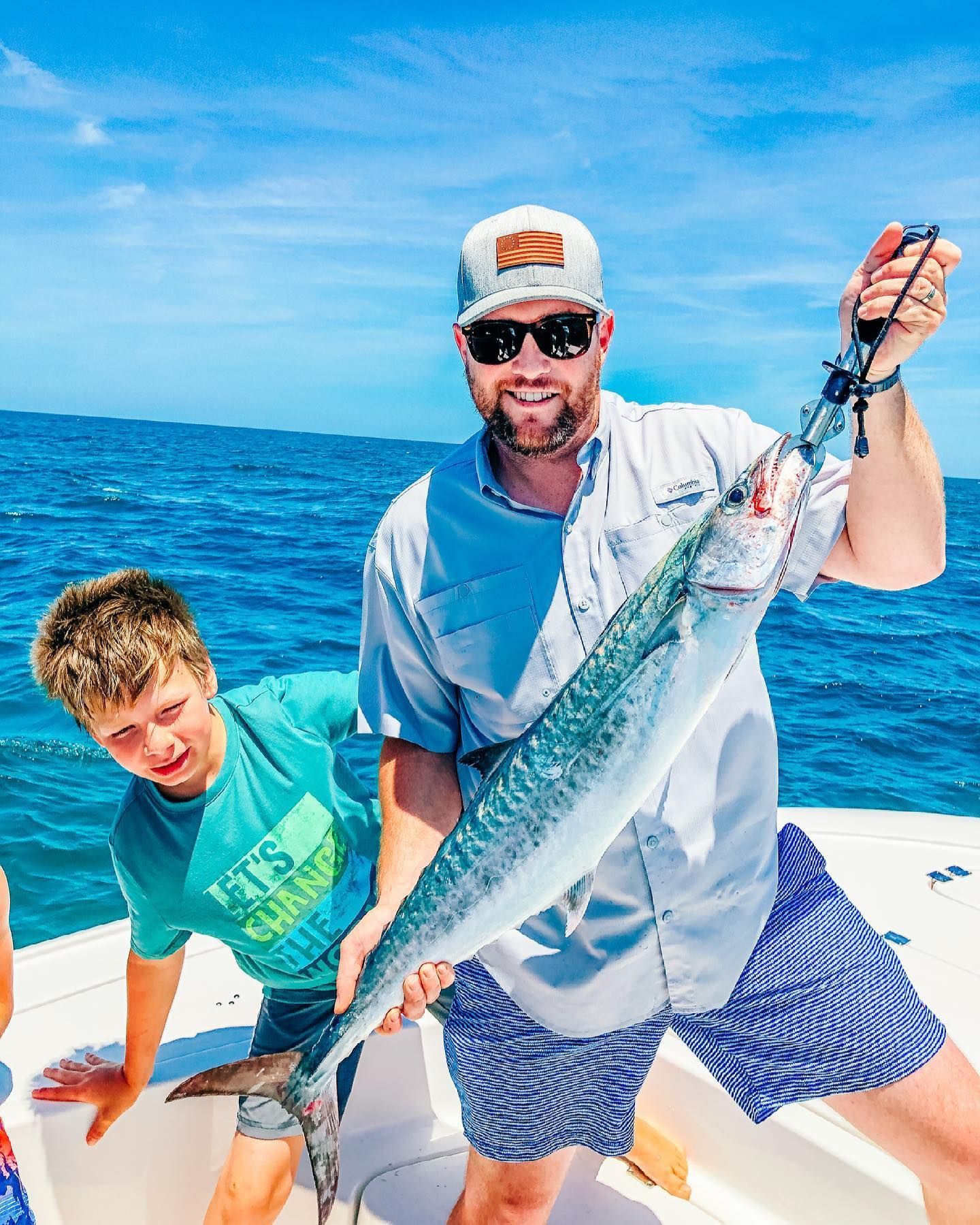 Man and boy on a boat, holding up a large fish, with ocean in the background.
