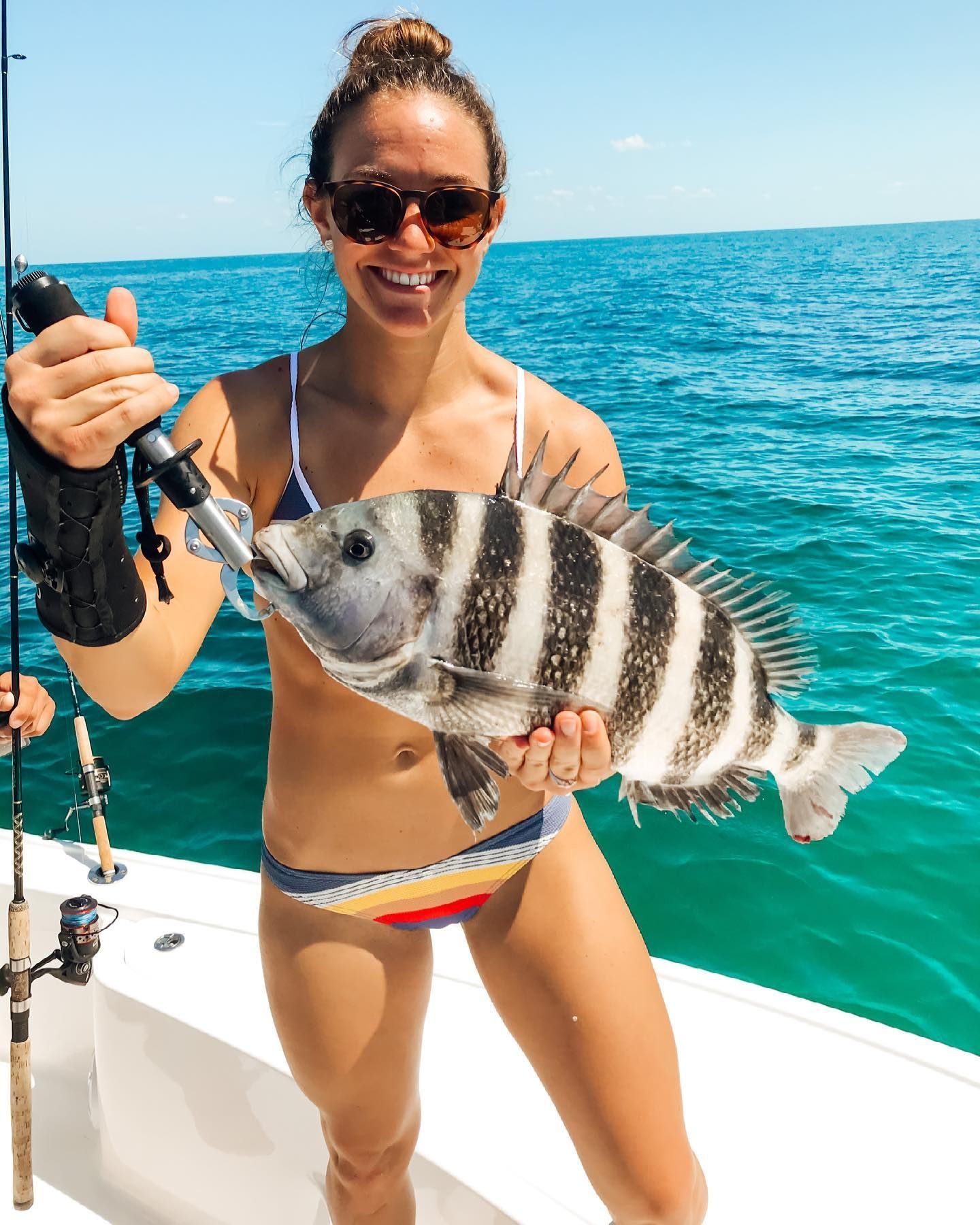 Woman smiles, holding striped fish caught on a boat, ocean background.