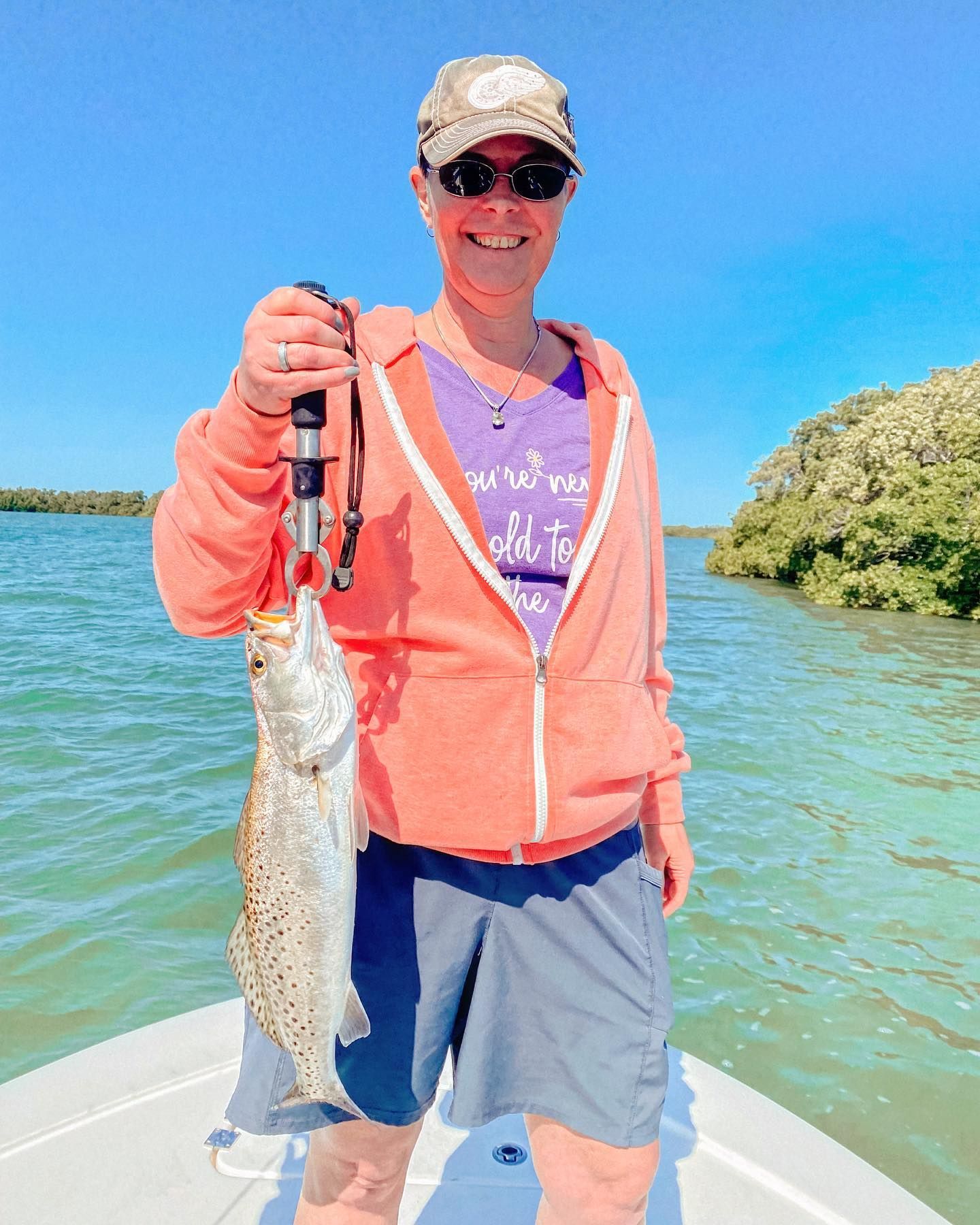 Woman on a boat holding a speckled trout, smiling. Sunny day on the water.