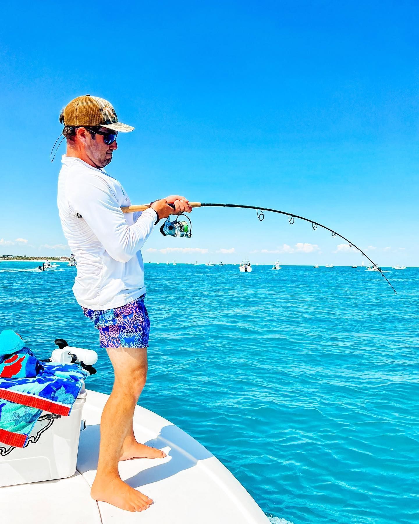 Man fishing from a boat on a sunny day, pulling on the rod. Bright blue water and sky.