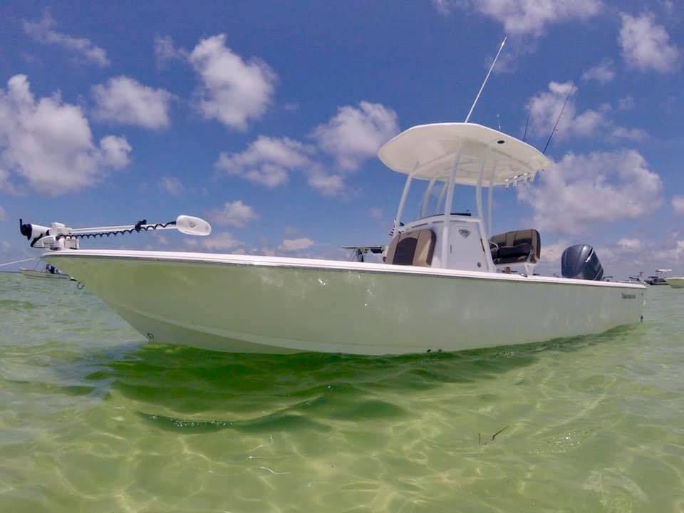 White fishing boat in shallow, clear water under a sunny, blue sky.