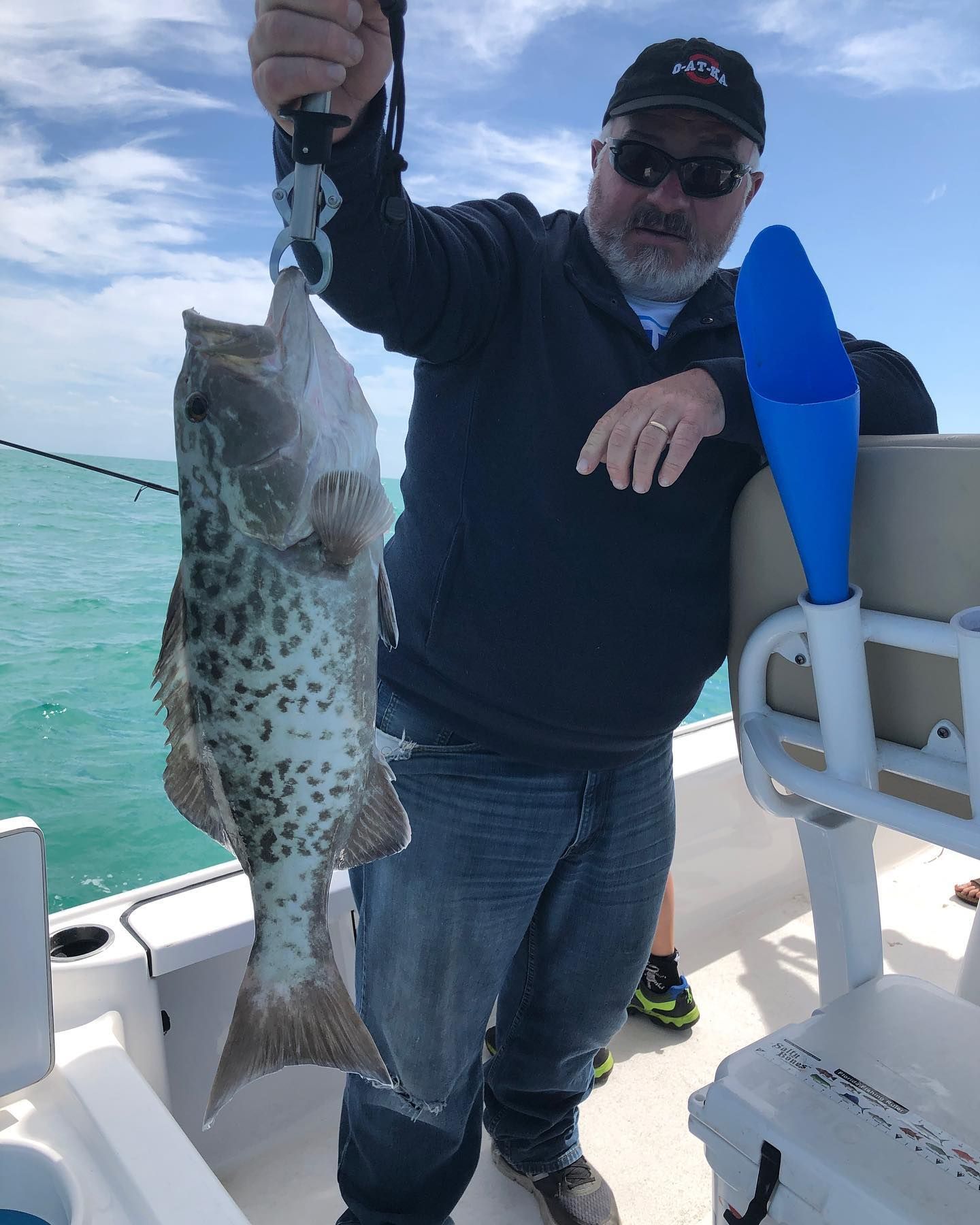 Man on boat holds up speckled fish, ocean background.