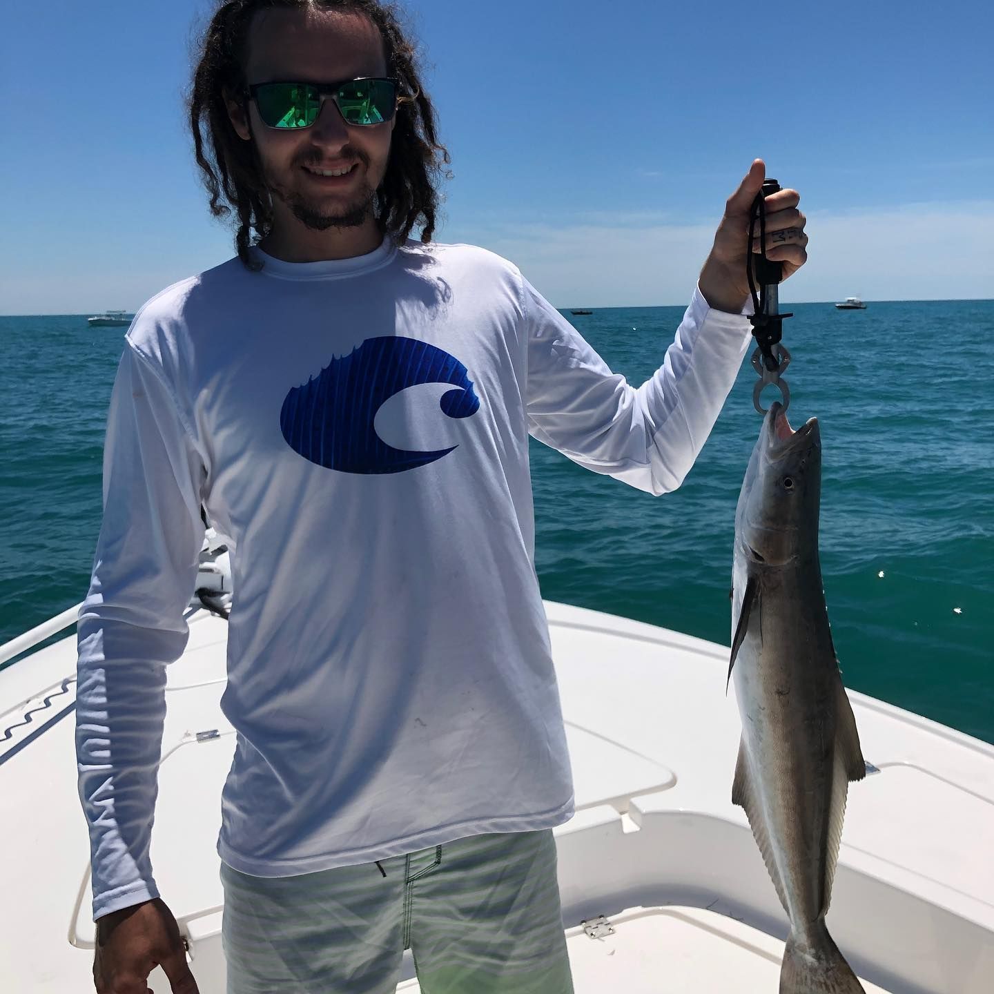 Man on boat holds up a fish, smiling, on a sunny day.
