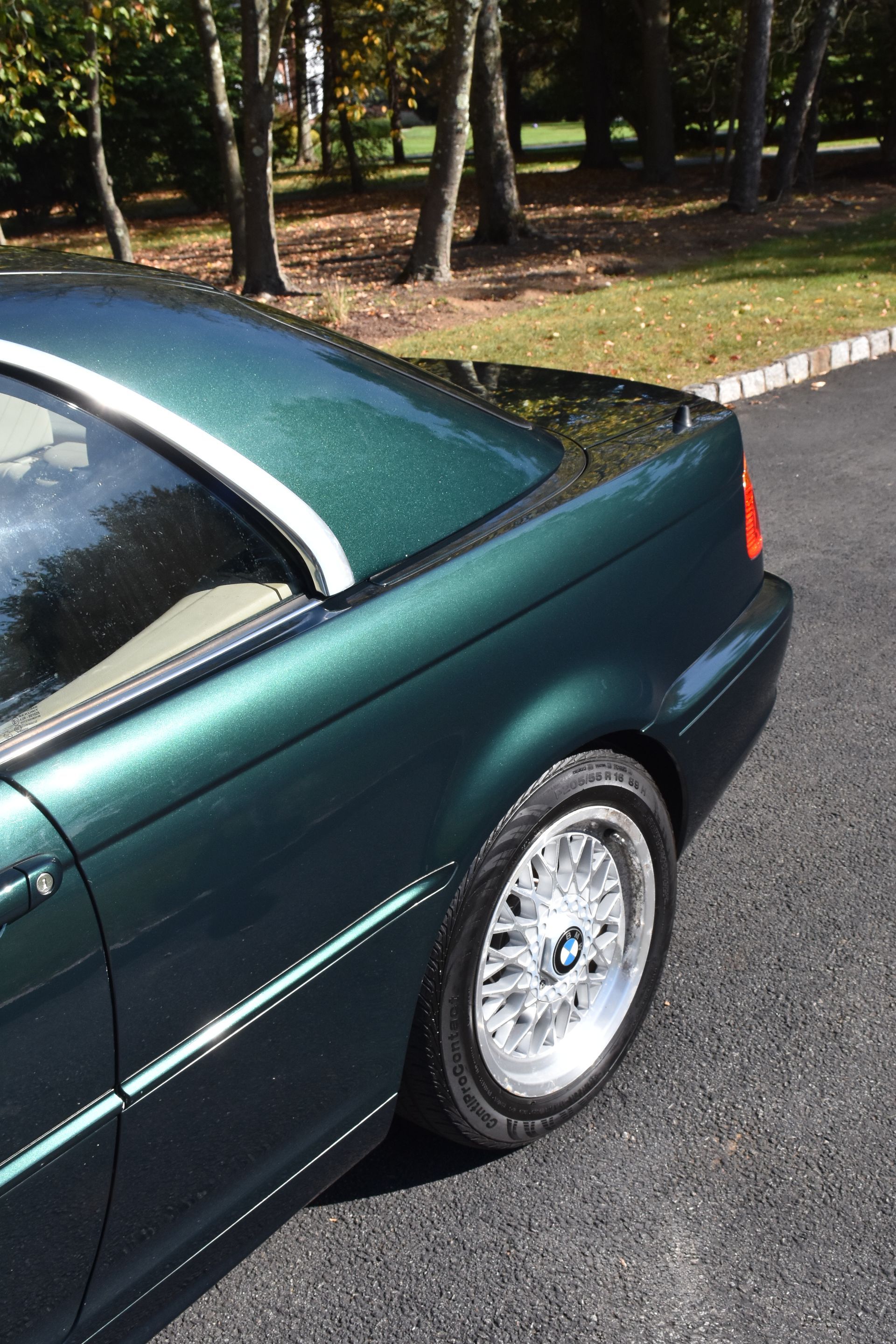 Green convertible car parked on asphalt, trees in background, silver rimmed wheel.