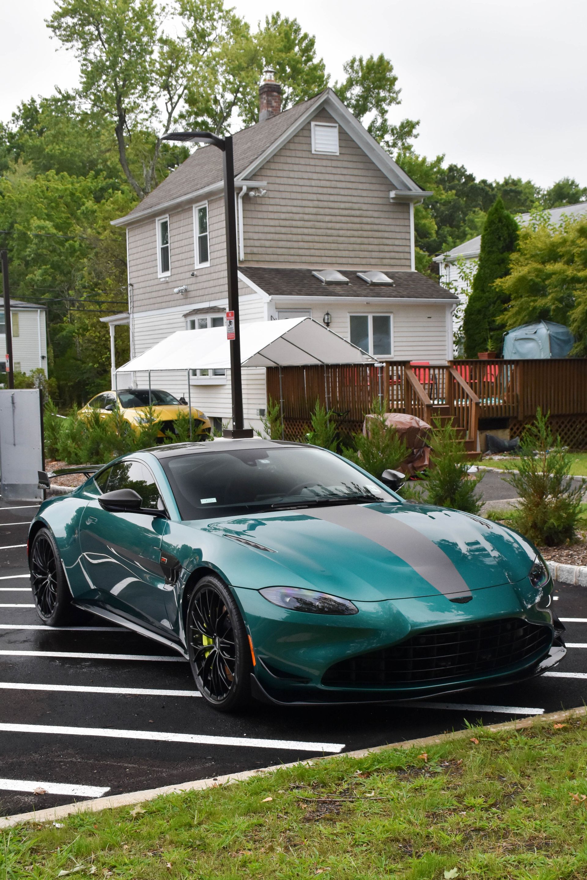 Green Aston Martin sports car parked in front of a house, with a black stripe down the hood.