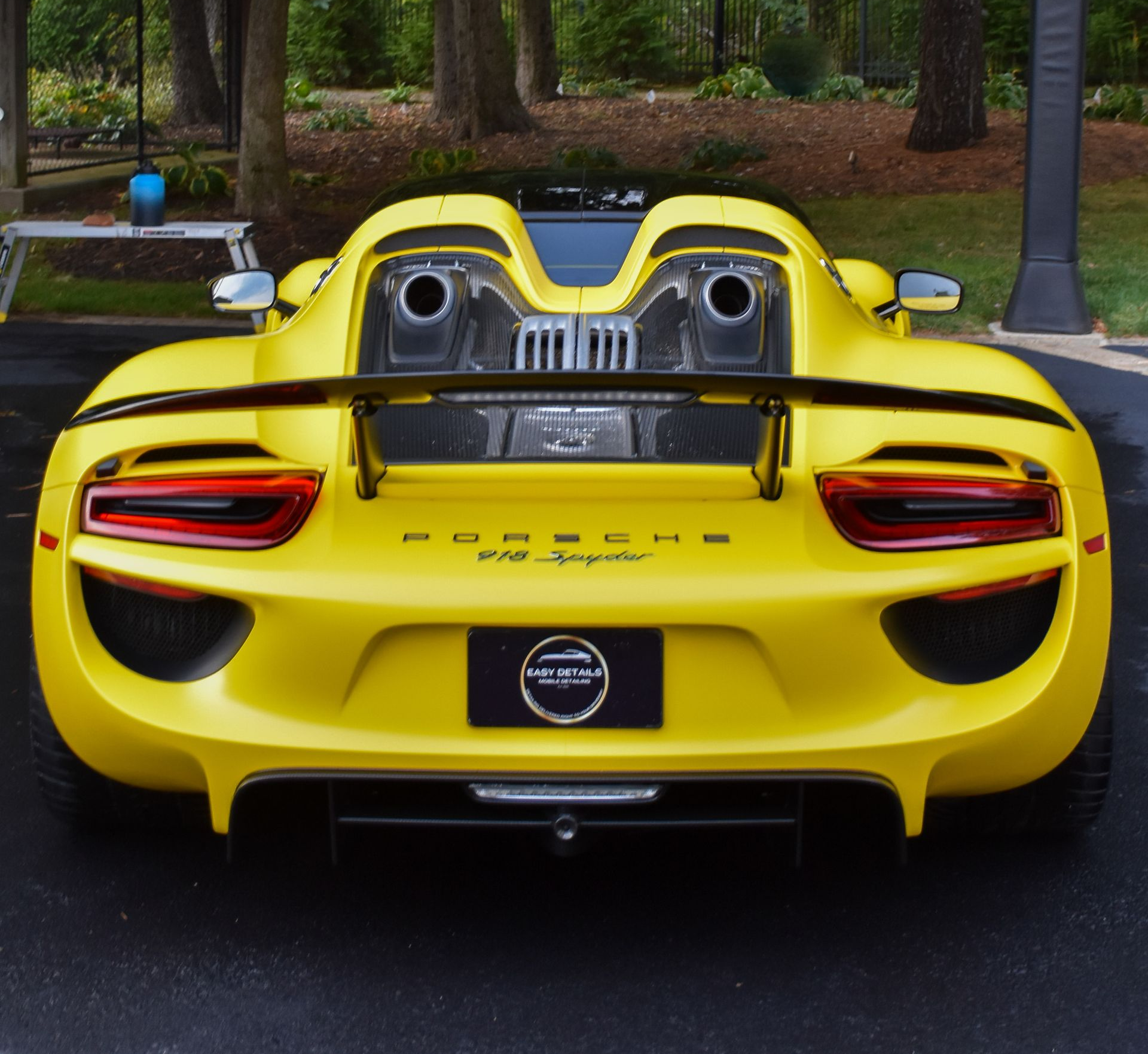 Yellow Porsche 918 Spyder sports car from the rear, with exposed engine components, black spoiler, and black license plate.