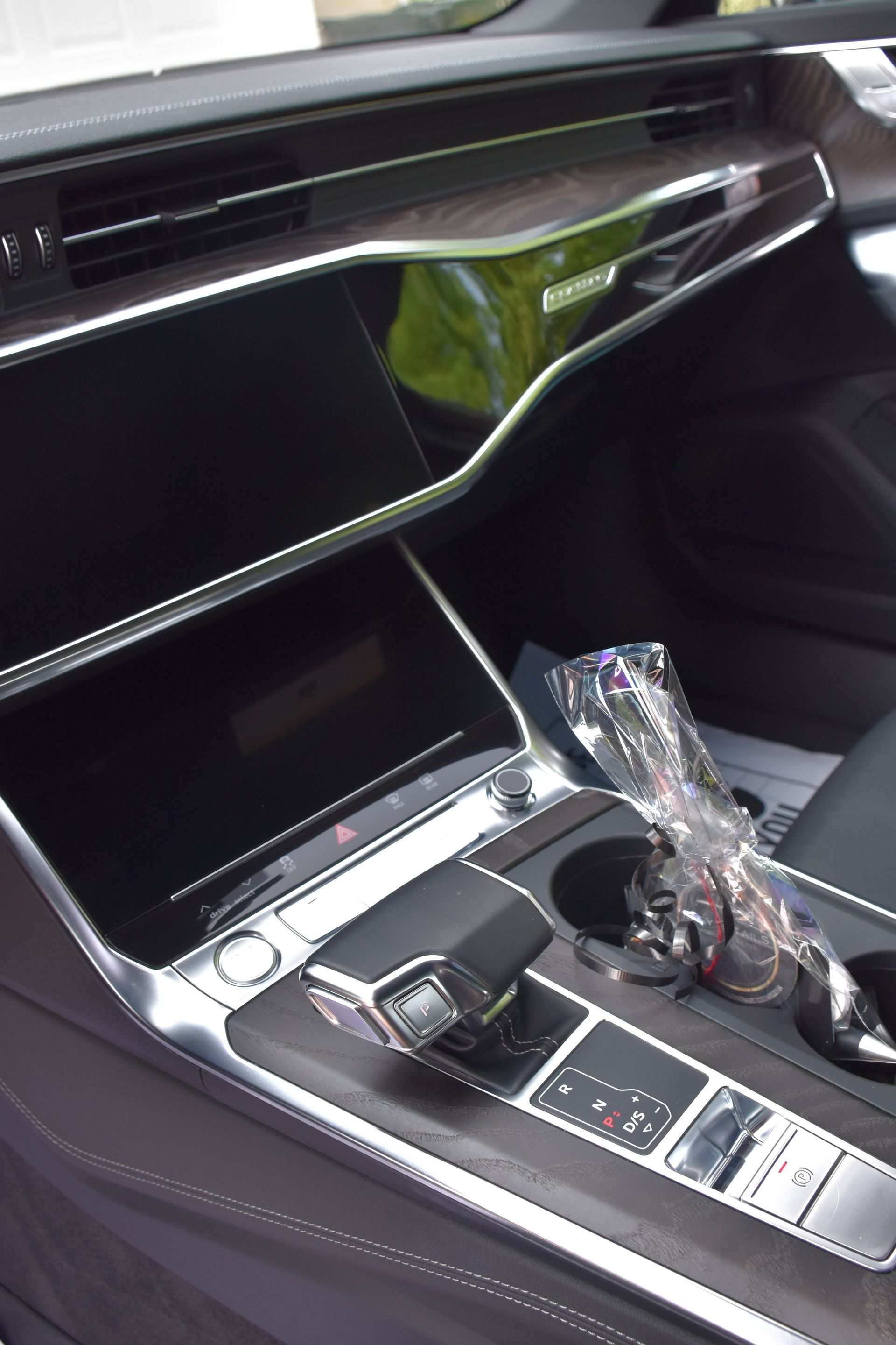 Interior of a modern car, featuring a dashboard with two large screens, a gear selector, and cup holders.